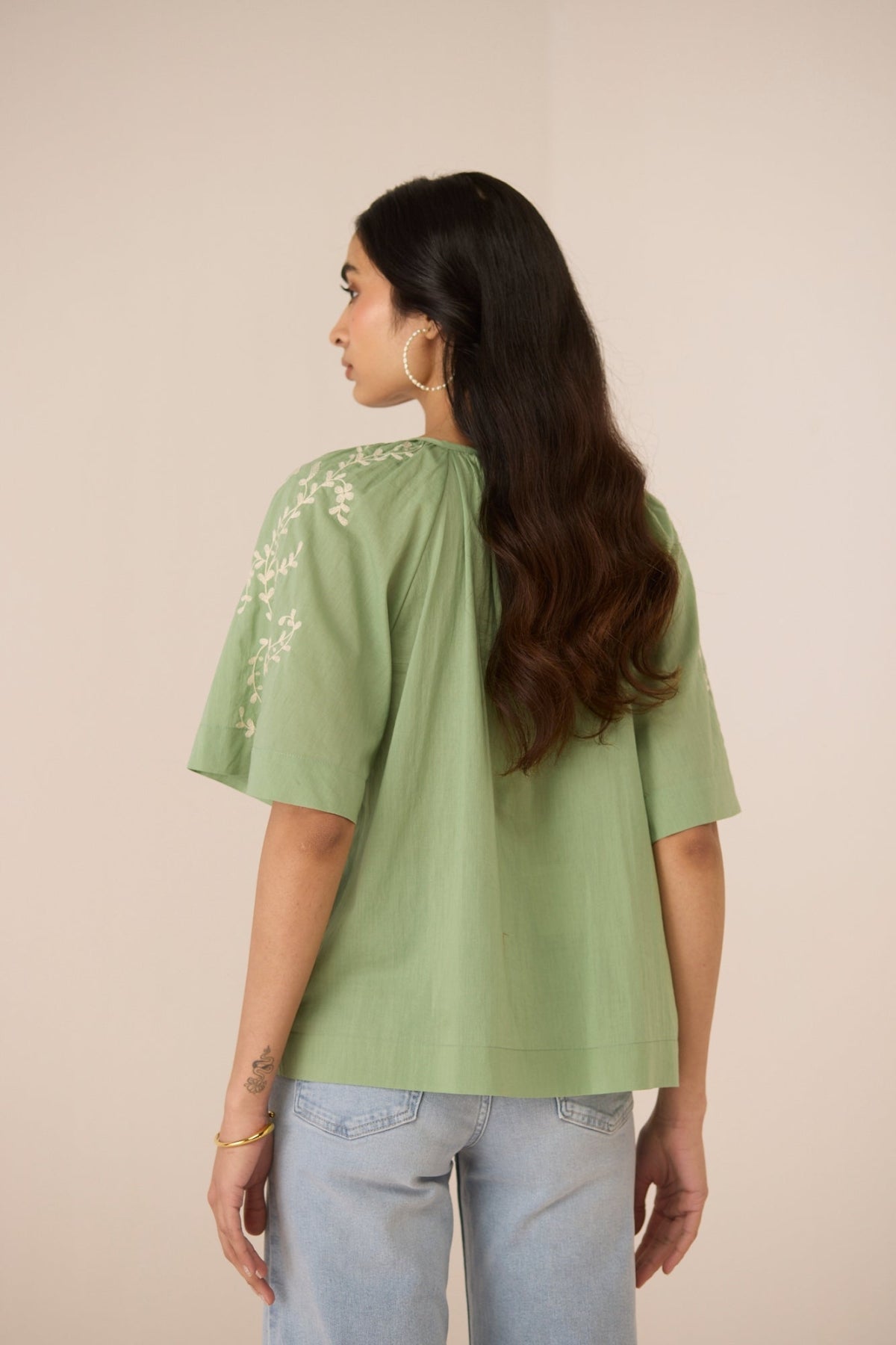 Woman wearing a green top with floral embroidery on a beige background Calling June