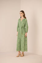 Woman wearing a green dress with floral patterns against a beige background Calling June