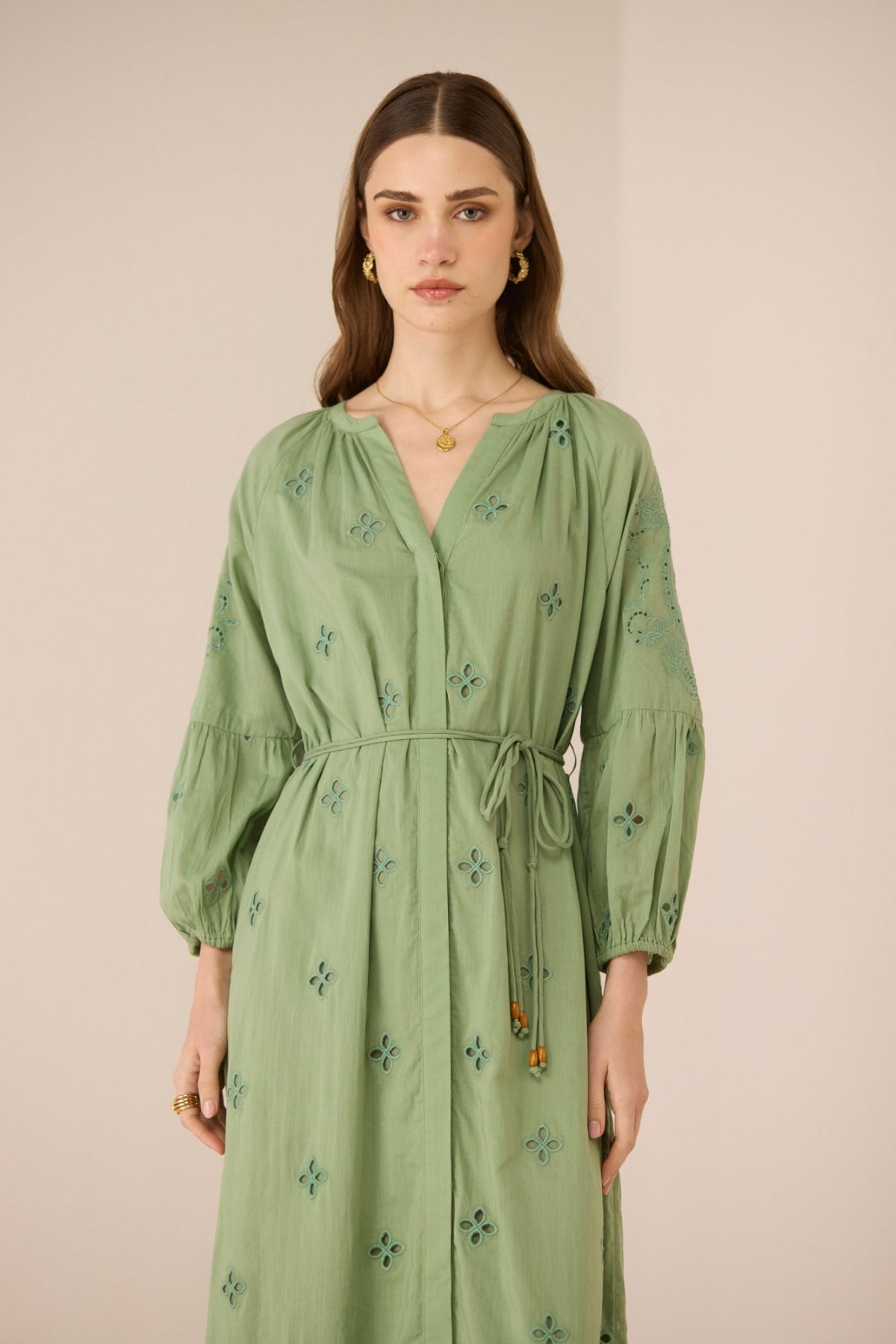 Woman wearing a green dress with floral embroidery against a beige background Calling June