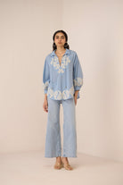 Woman wearing a light blue embroidered outfit on a beige background Calling June