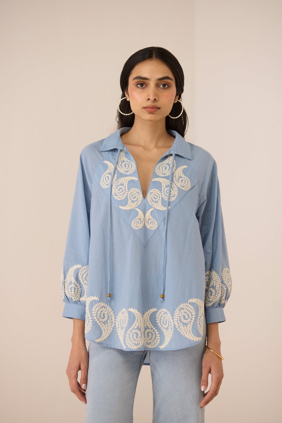 Woman wearing a light blue embroidered blouse against a beige background Calling June