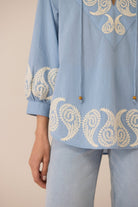 Light blue blouse with intricate white embroidery on a beige background Calling June