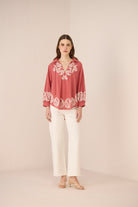Woman wearing a red embroidered blouse and white pants on a beige background Calling June