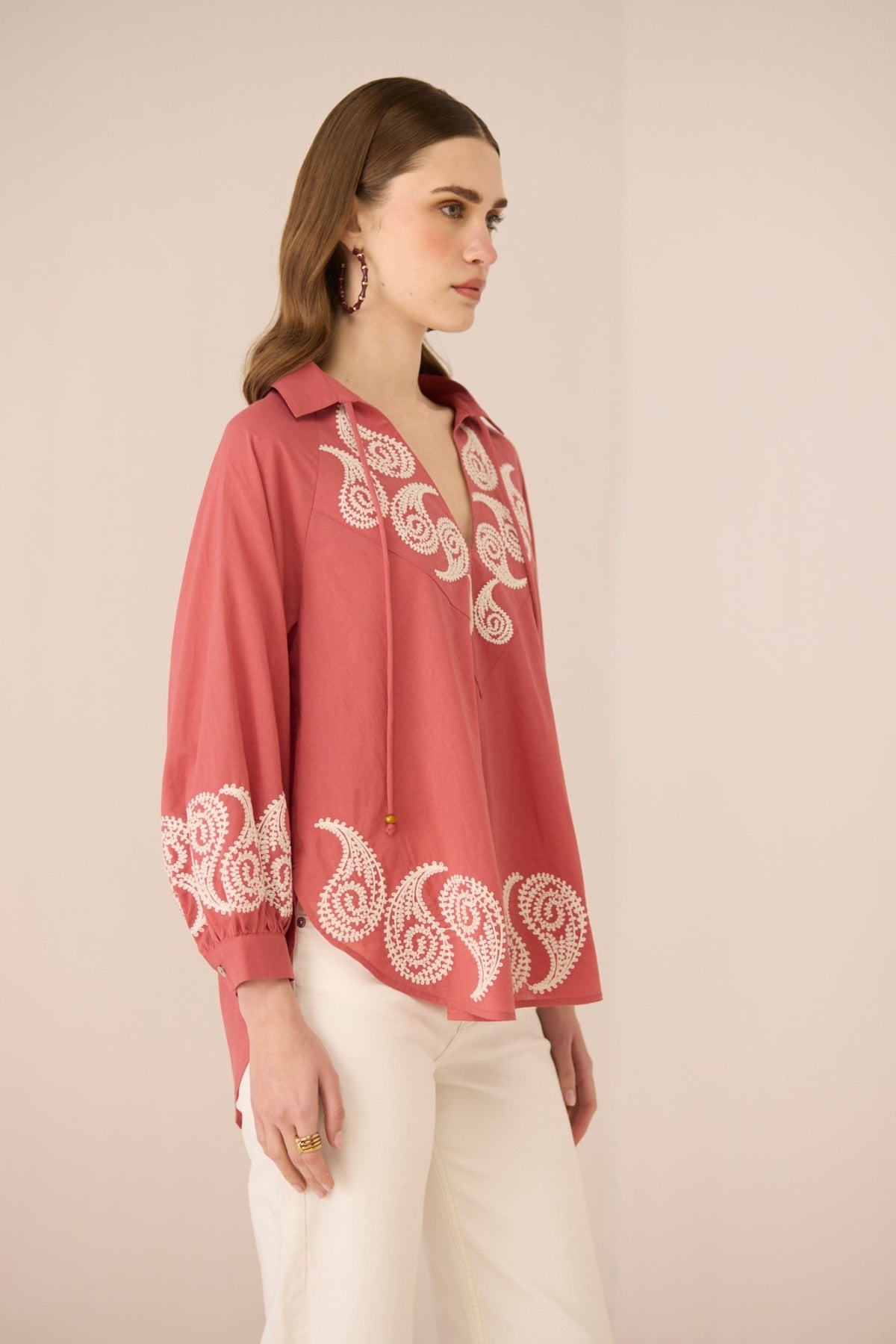 Woman wearing a pink blouse with white embroidery on a beige background Calling June