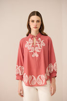 Woman wearing a red blouse with white embroidery on a beige background Calling June