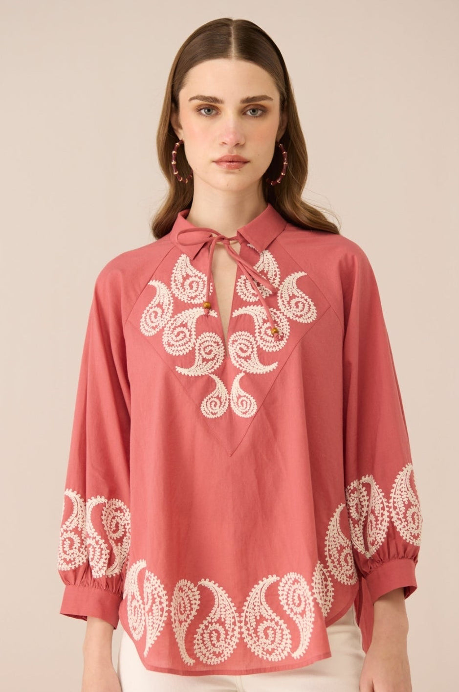 Woman wearing a red blouse with white embroidery on a beige background Calling June