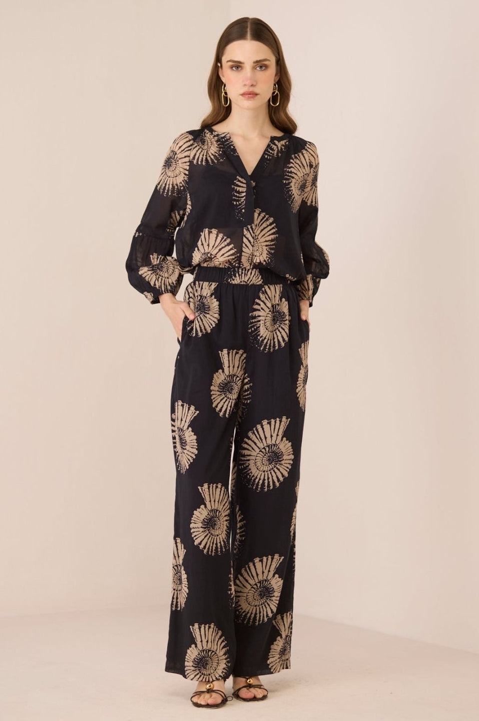 Woman wearing a black jumpsuit with gold sunflower patterns on a beige background Calling June