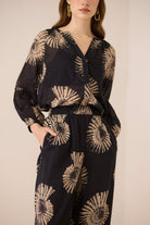 Woman wearing a black outfit with gold floral patterns on a beige background Calling June