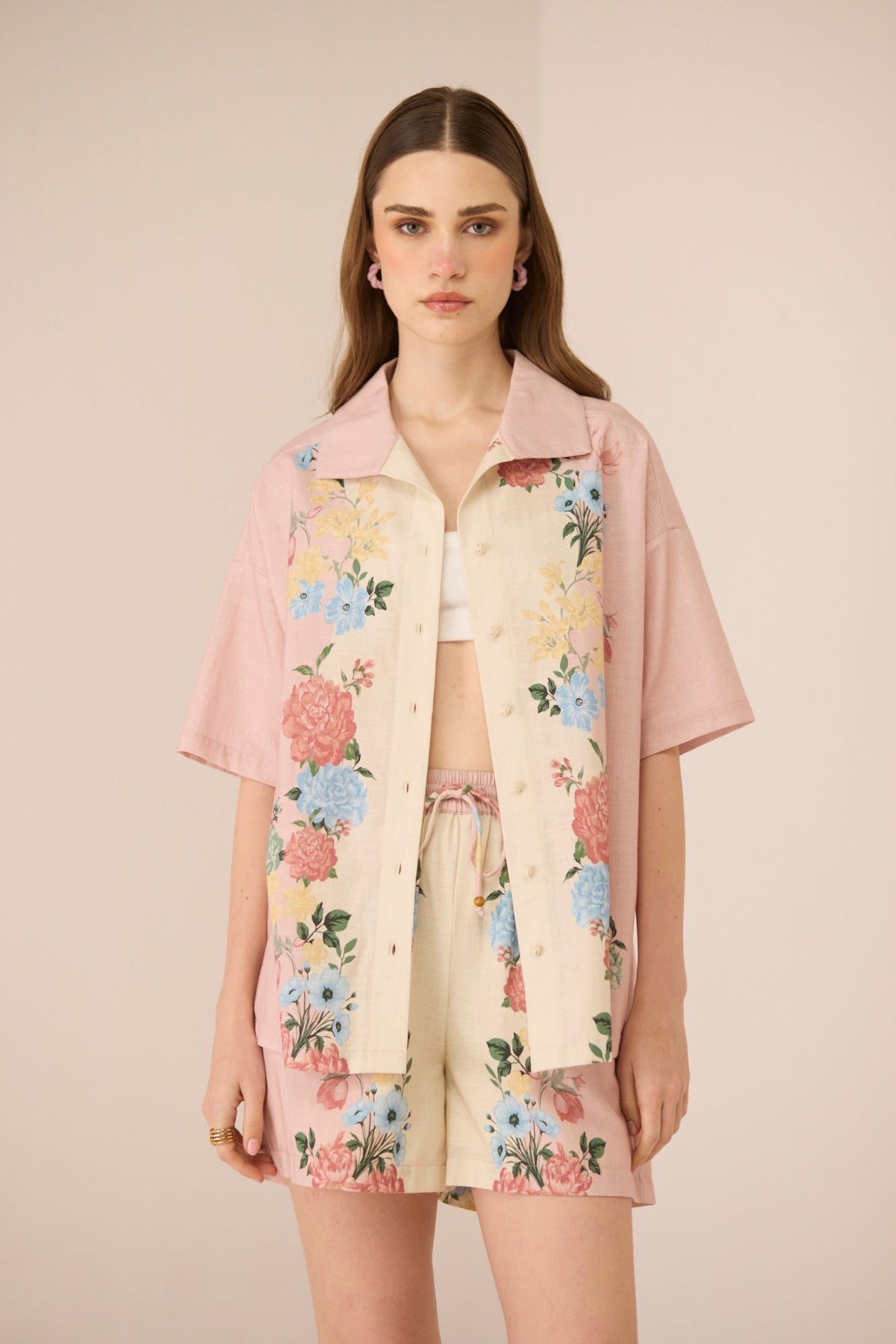 Woman wearing a floral shirt and shorts set with a pink jacket on a beige background Calling June