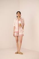 Woman wearing a light pink outfit with a matching jacket on a plain background Calling June