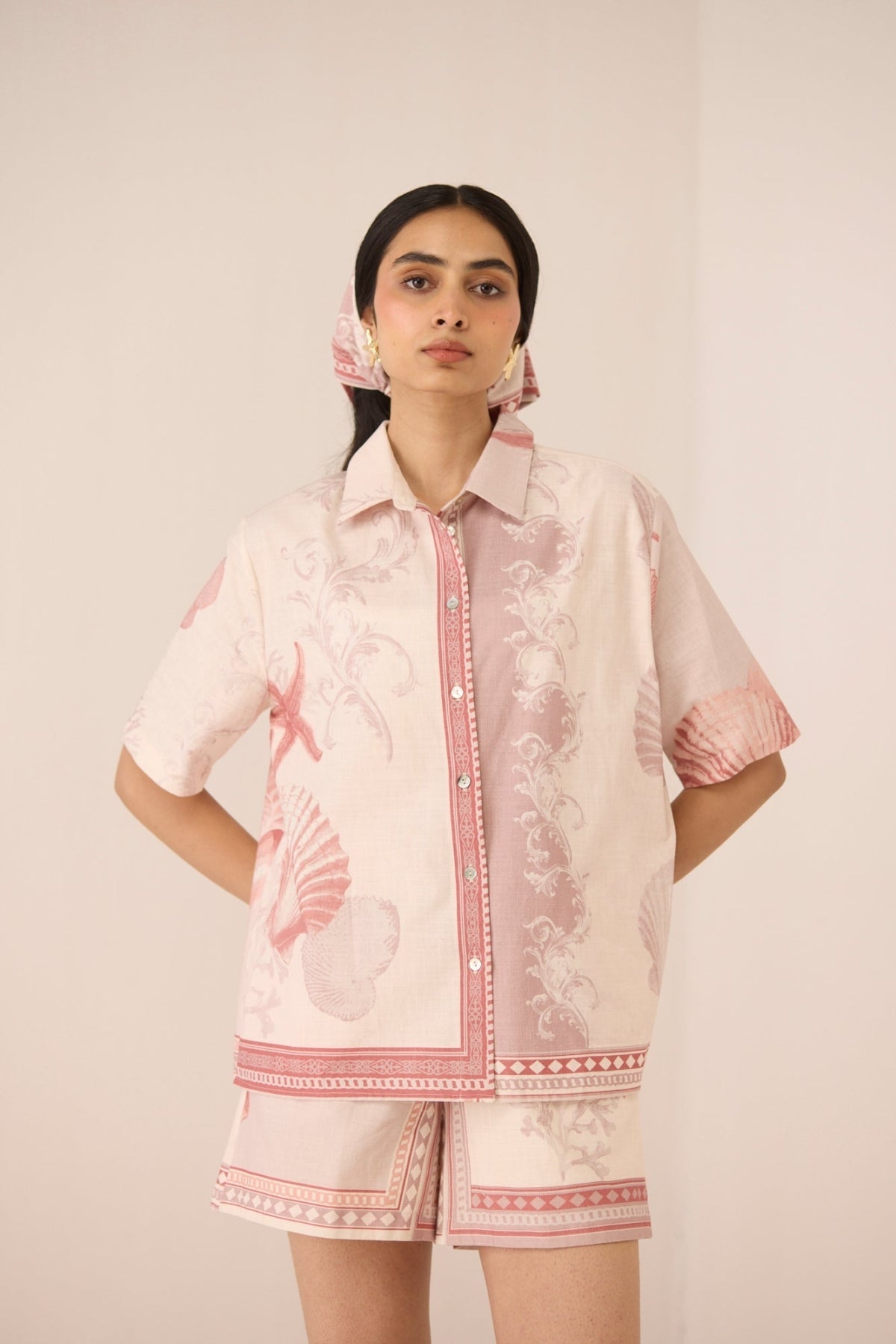 Woman wearing a matching pink and white outfit with floral patterns on a plain background Calling June