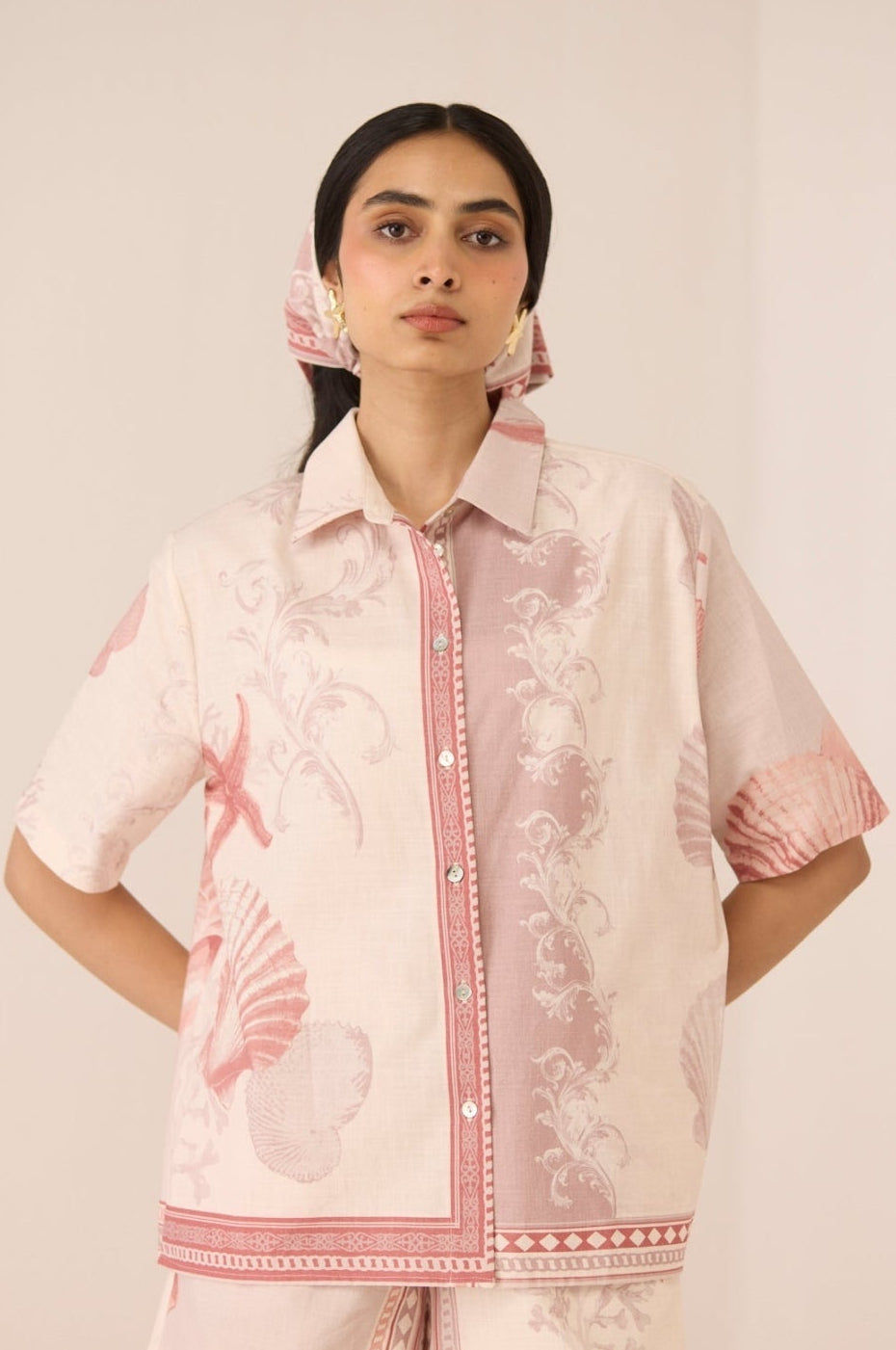 Woman wearing a matching pink and white outfit with floral patterns on a plain background Calling June