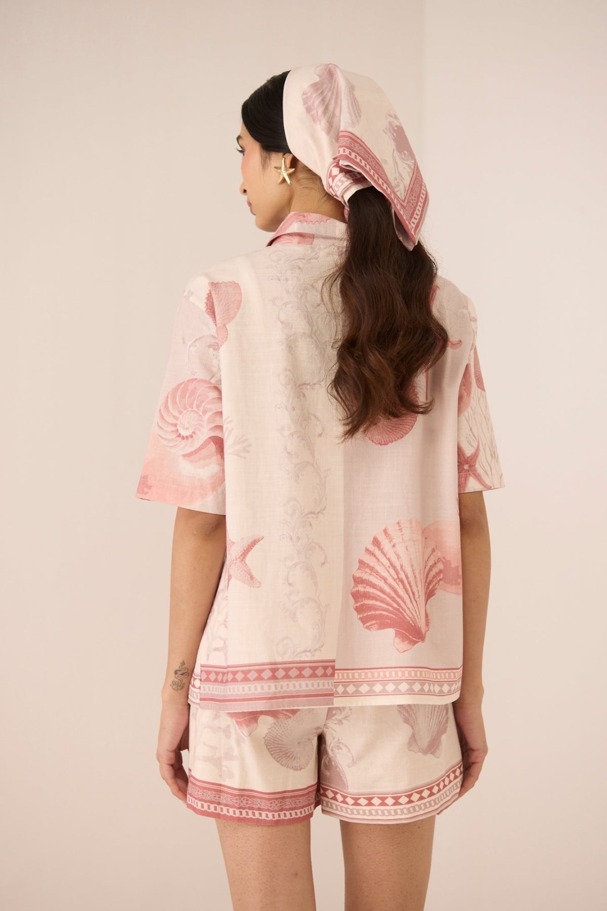 Woman wearing a matching top and shorts set with pink shell patterns on a beige background Calling June