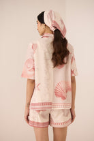 Woman wearing a matching top and shorts set with pink shell patterns on a beige background Calling June