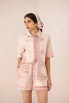 Woman wearing a pink and white patterned outfit with a matching headscarf against a beige background Calling June