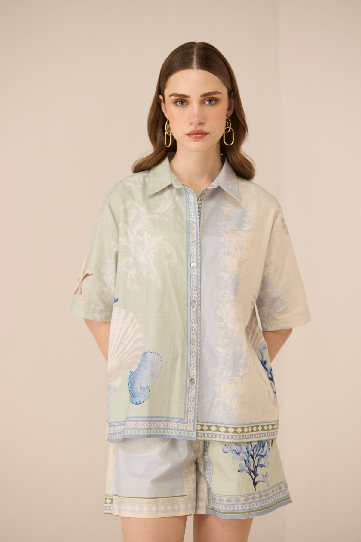 Woman wearing a light green and beige floral patterned shirt with matching shorts on a beige background Calling June