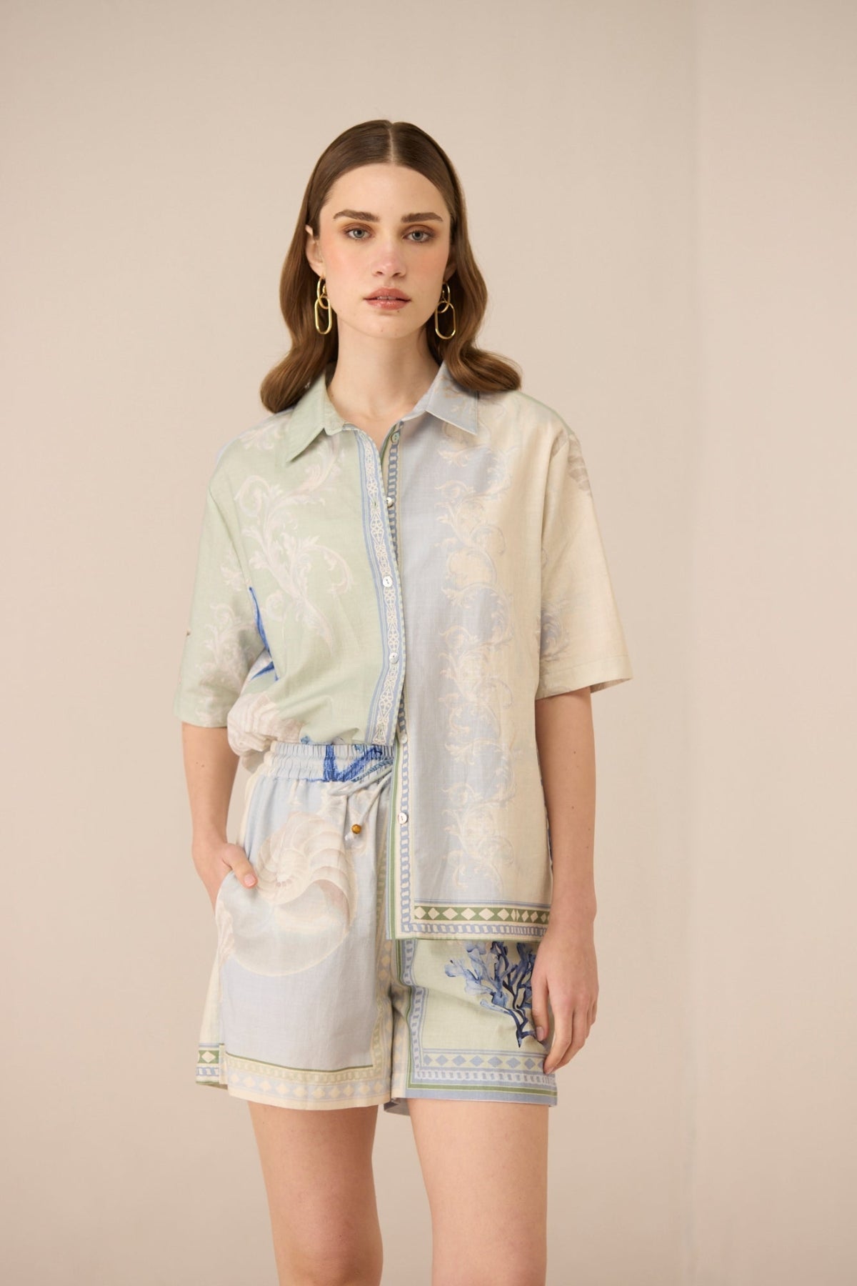 Woman wearing a light-colored shirt with a patterned skirt against a plain background Calling June