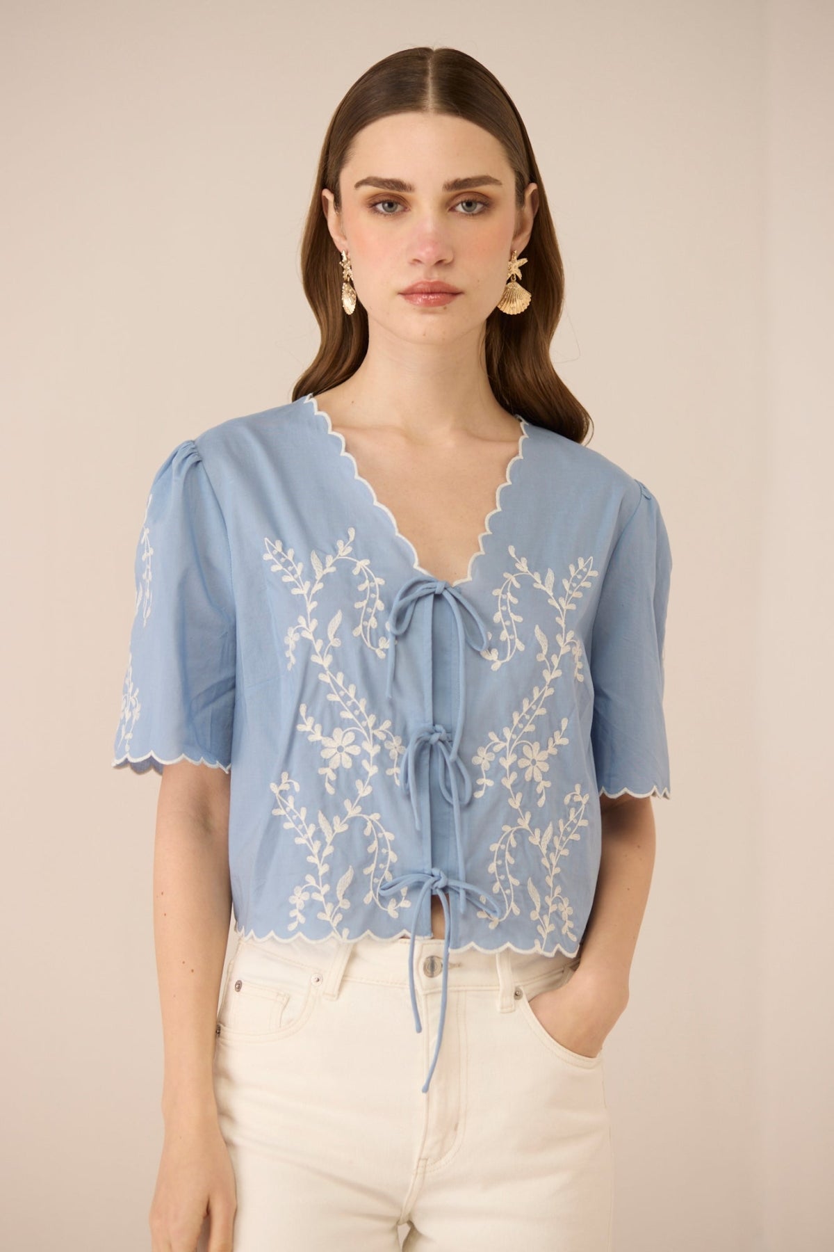 Woman wearing a light blue blouse with lace details on a beige background Calling June