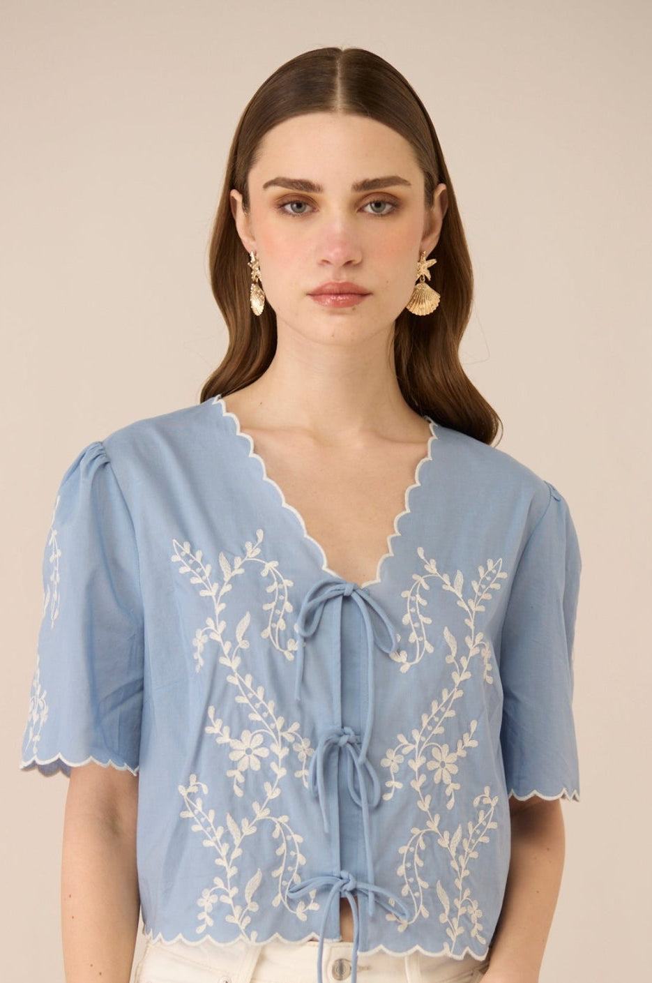 Woman wearing a light blue blouse with lace details on a beige background Calling June