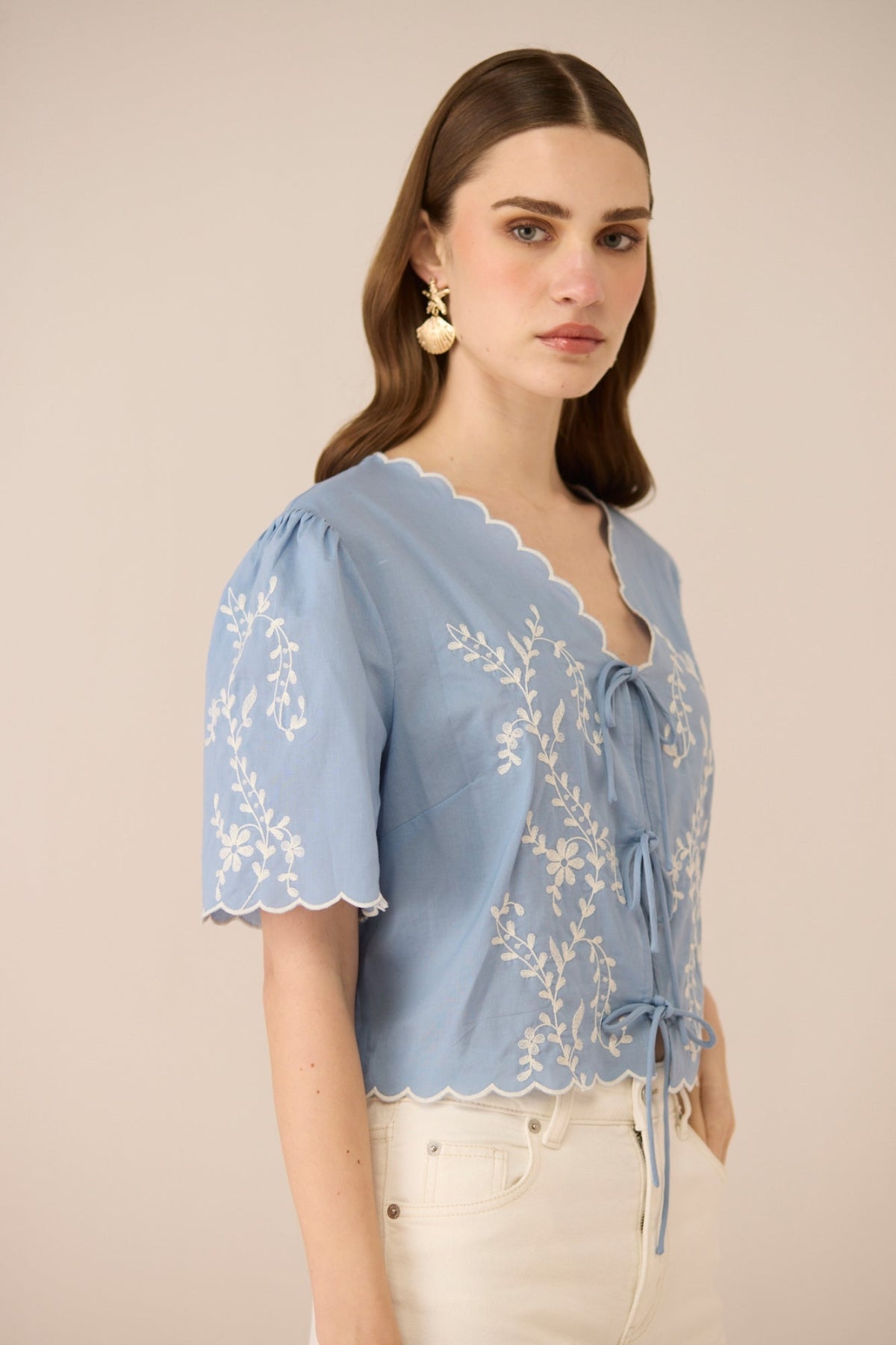 Woman wearing a light blue embroidered blouse against a beige background Calling June