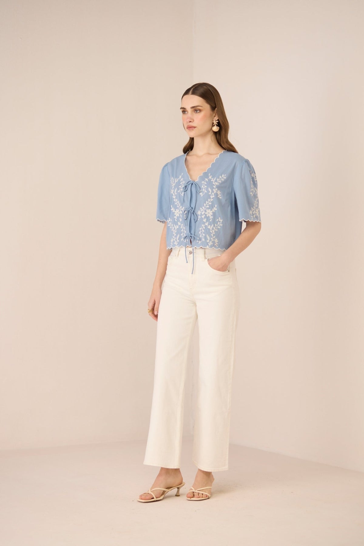 Woman wearing a blue floral blouse and white pants on a beige background Calling June