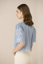 Woman wearing a light blue blouse with white embroidery on a beige background Calling June