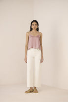 Woman wearing a pink top and white pants on a plain background Calling June