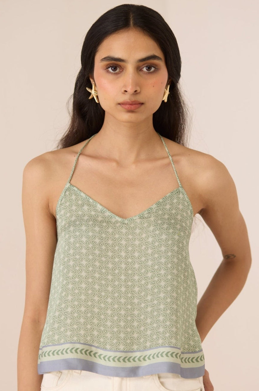 Woman wearing a green patterned top with white pants against a beige background Calling June