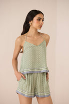 Woman wearing a green patterned top and shorts set against a beige background Calling June