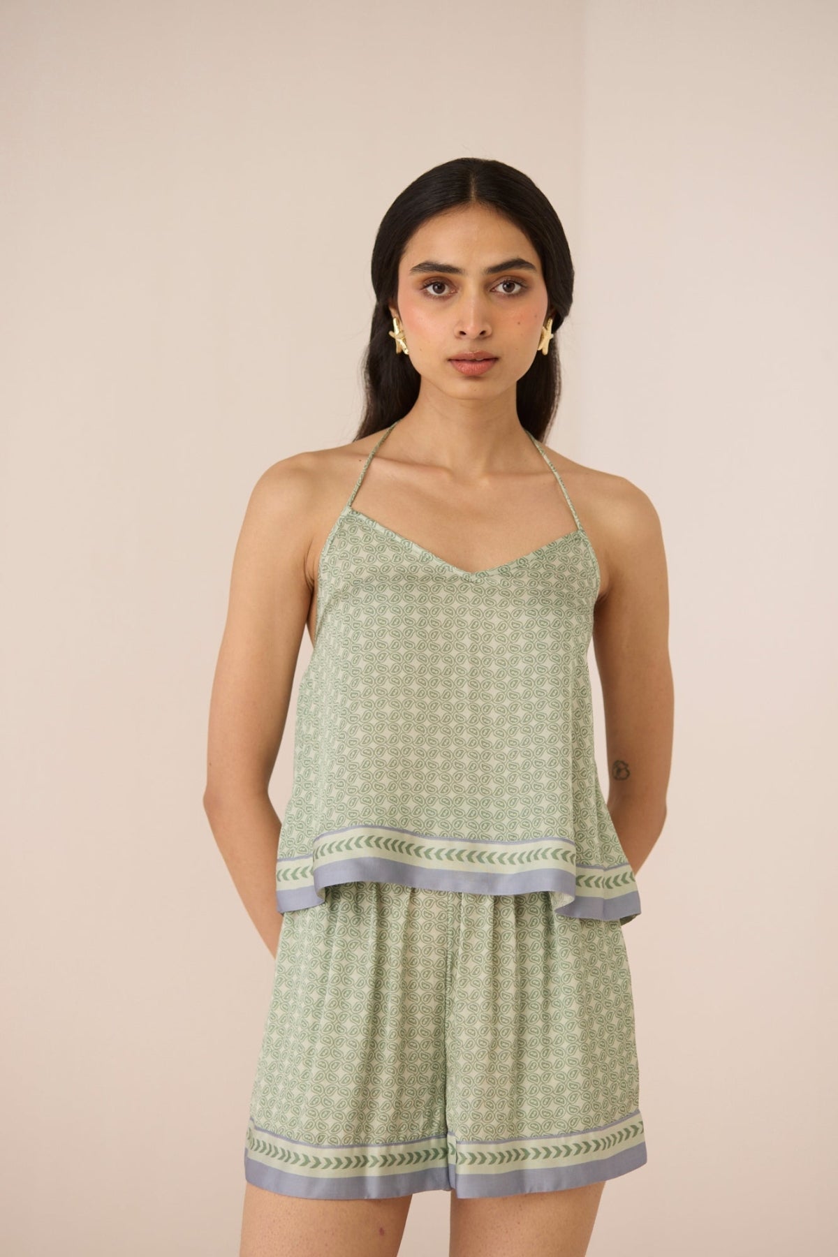 Woman wearing a green patterned top and shorts set on a beige background Calling June