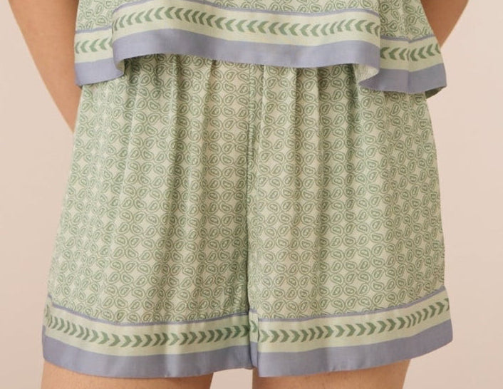 Woman wearing a green patterned top and shorts set on a beige background Calling June