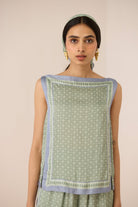 Woman wearing a green sleeveless top with a patterned border against a beige background Calling June