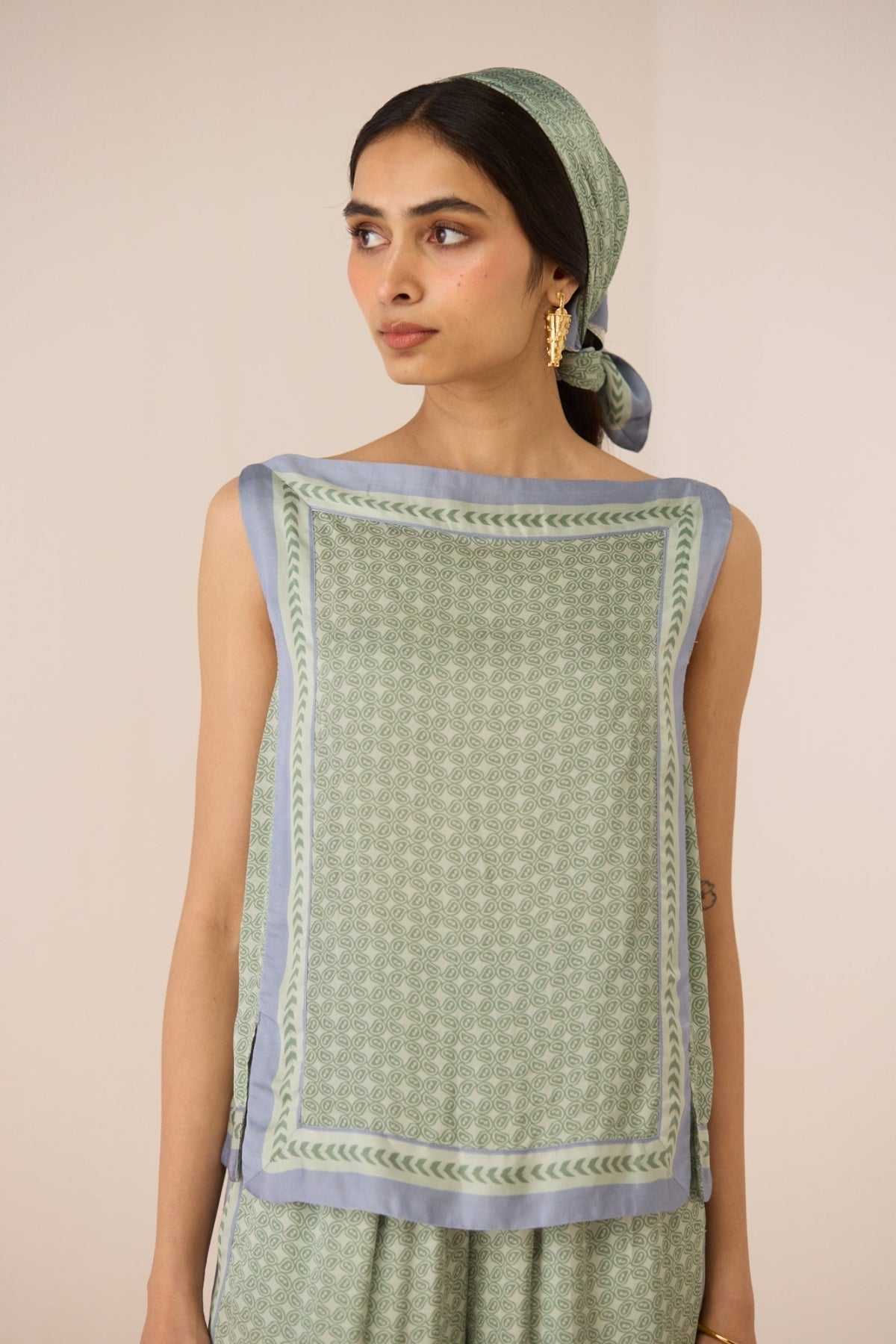 Woman wearing a green patterned outfit with a matching headscarf against a beige background Calling June