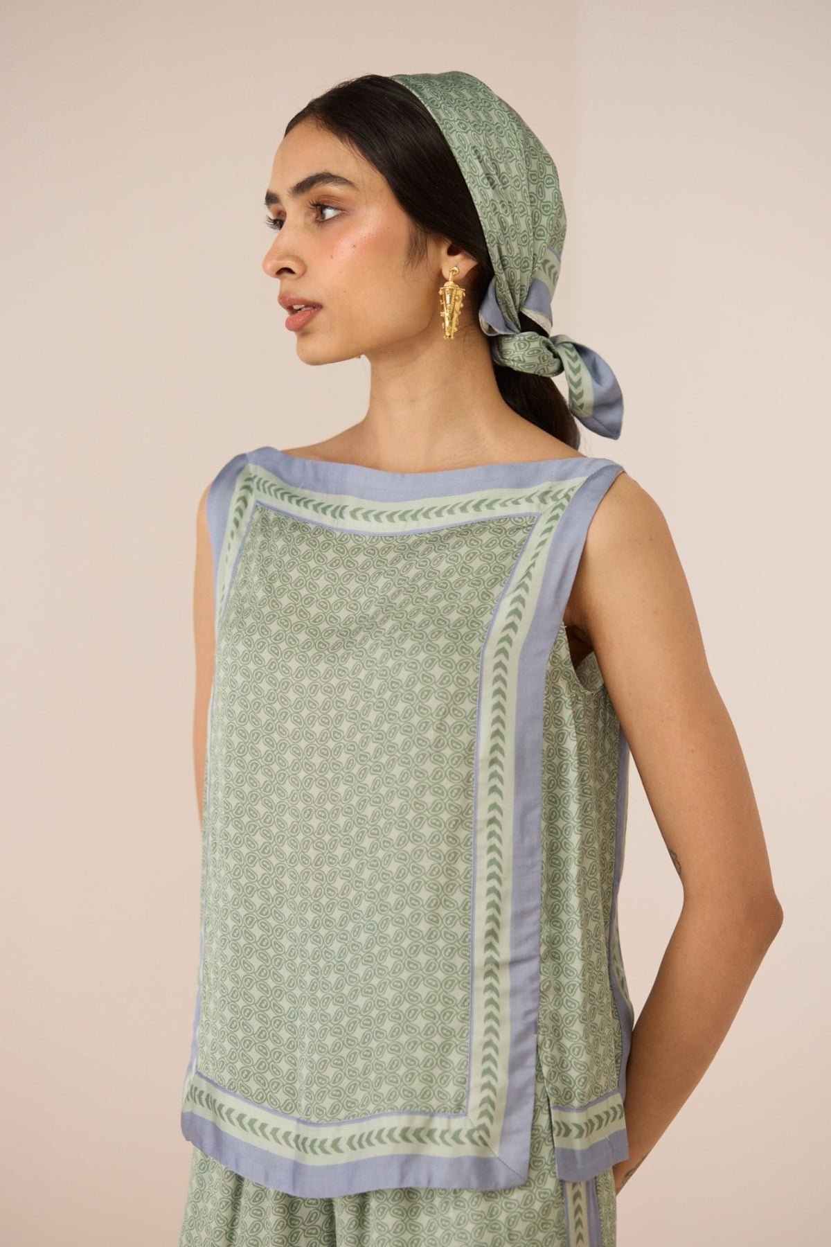 Woman wearing a green and blue patterned outfit with a matching headscarf against a beige background Calling June