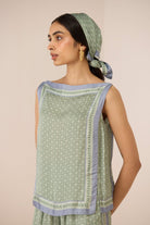 Woman wearing a green and blue patterned outfit with a matching headscarf against a beige background Calling June