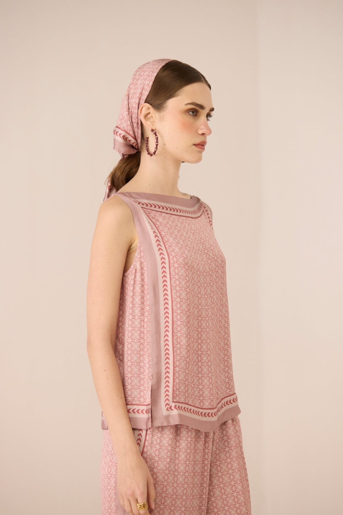 Woman wearing a pink patterned top and headscarf against a beige background Calling June
