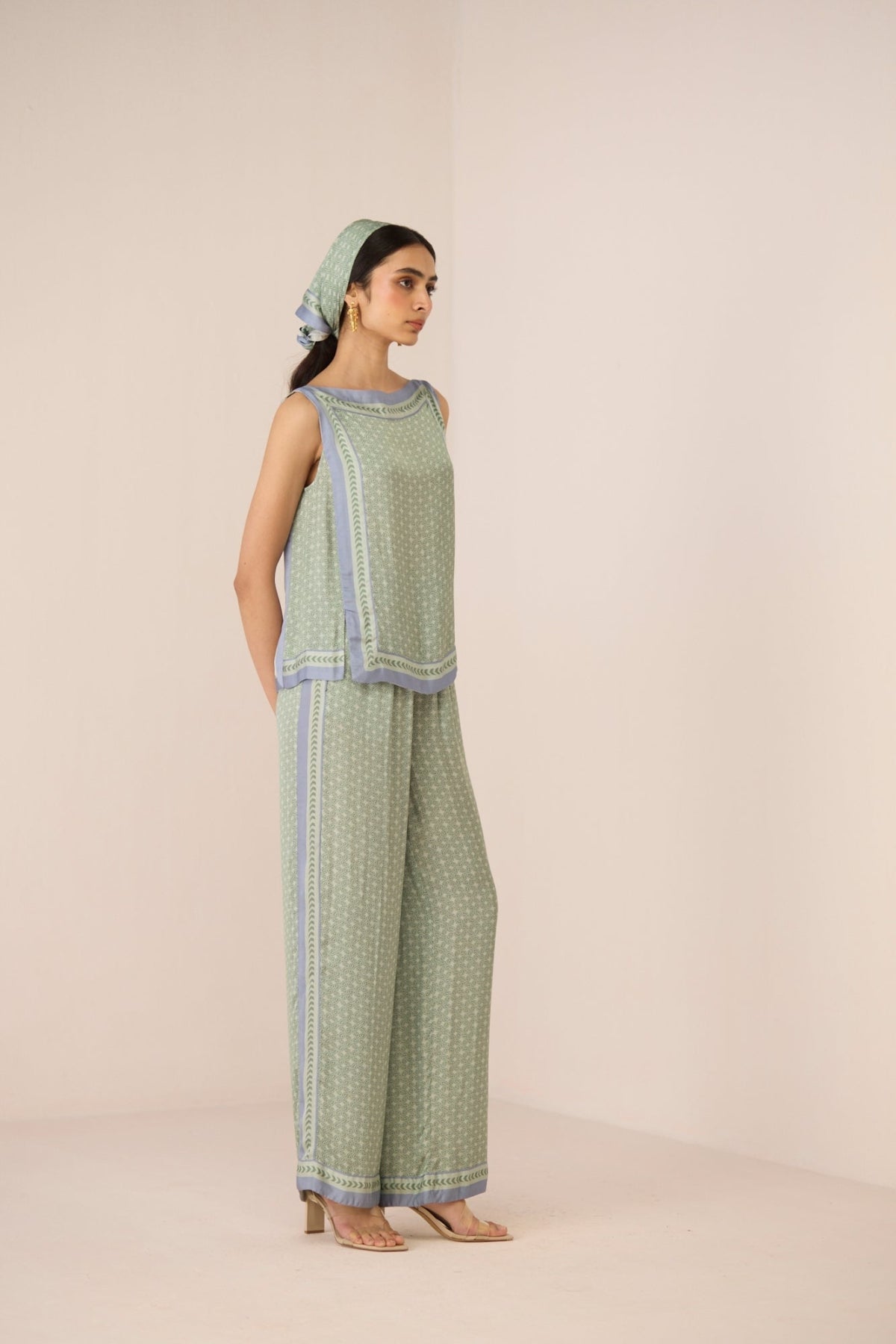 Woman wearing a green patterned outfit with a matching headscarf on a beige background Calling June